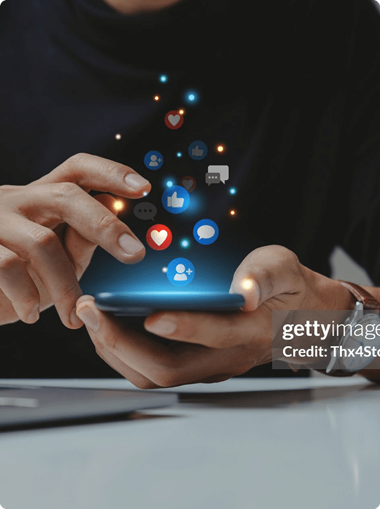 A person uses a smartphone with social media notification icons, such as likes, messages, and hearts, appearing above the device.